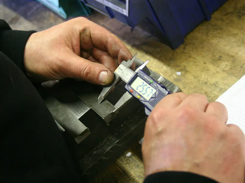 Inspector measuring a machined part with a digital caliper